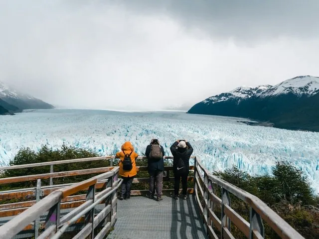 Des touristes contemplent l'immense glacier Spegazzini, d'un bleu glacé, depuis une passerelle en bois.