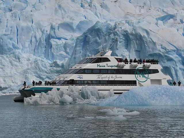 A tour boat navigates through icy waters close to the towering glacier face.