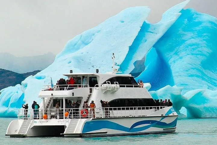 Los turistas en un barco admiran un enorme iceberg esculpido en el lago glaciar.