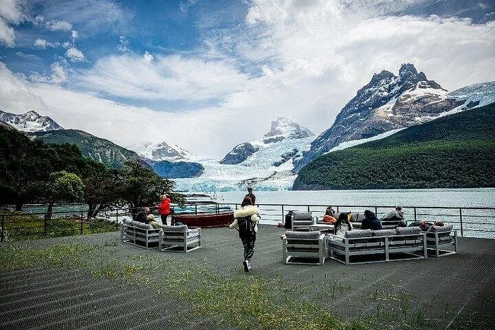 La gente se relaja en muebles de descanso en una cubierta exterior con vistas al glaciar.