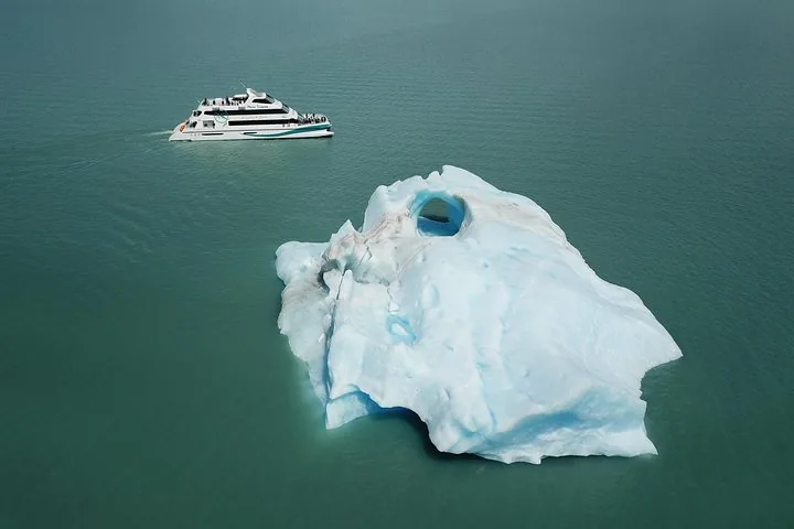 Eine Luftaufnahme eines Tourboots, das sich einem großen, schwimmenden Eisberg nähert.