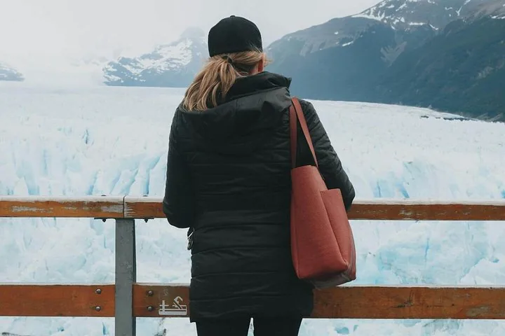 Une femme se tient à une rambarde et observe la glace glaciaire d'un bleu saisissant.