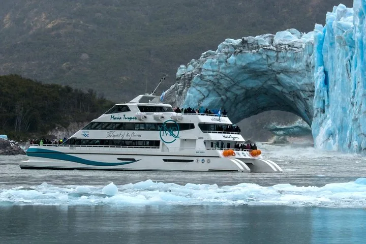 Een grote tourboot vaart langs een indrukwekkende natuurlijke ijsboog.